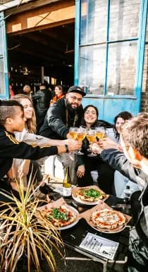 Gasten proosten boven een tafel met versgebakken pizza's