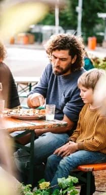 Een gast deelt een pizza met een kind aan een lange tafel