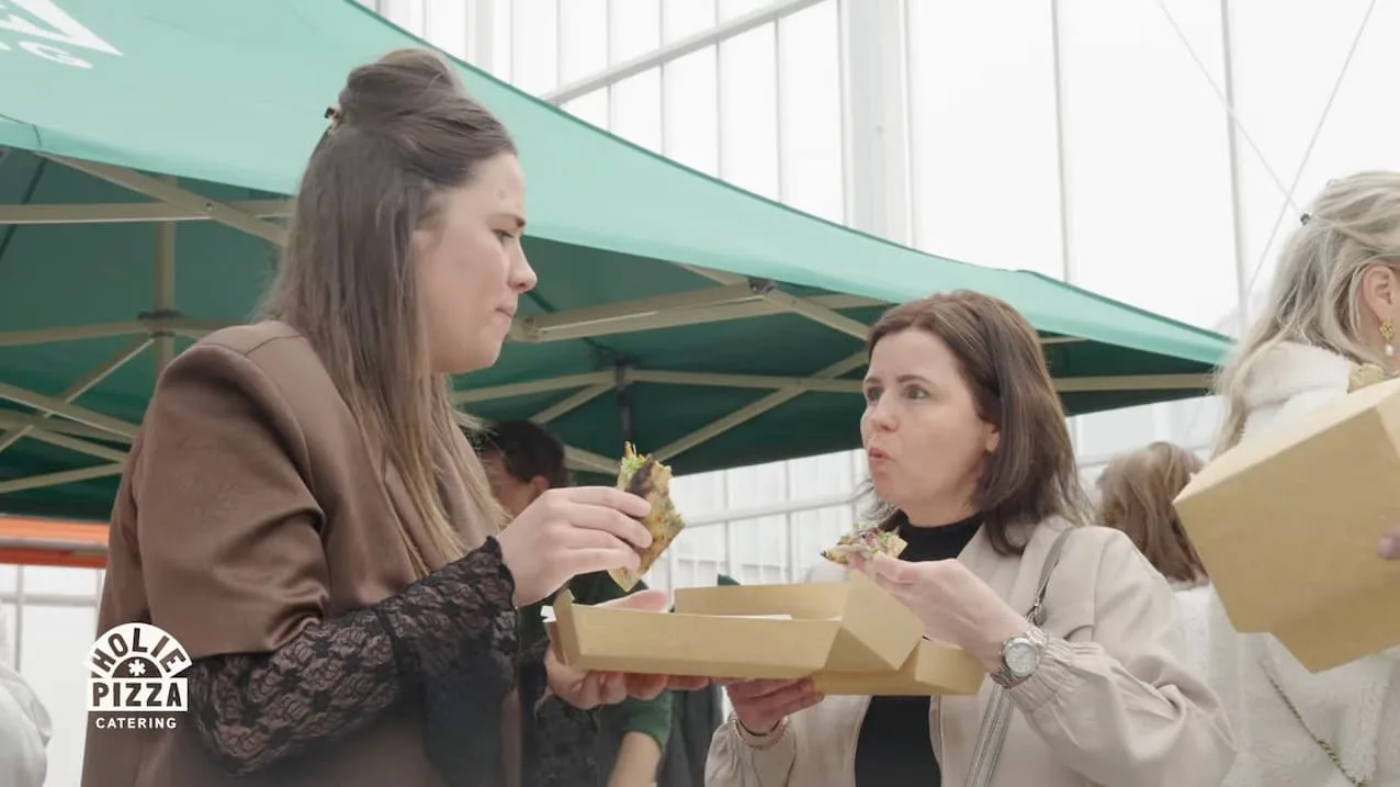 Twee gasten eten een punt pizza onder de groene partytent
