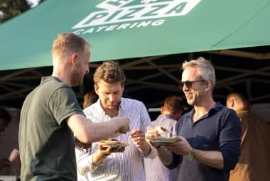 Drie gasten met een bordje pizza onder de groene partytent