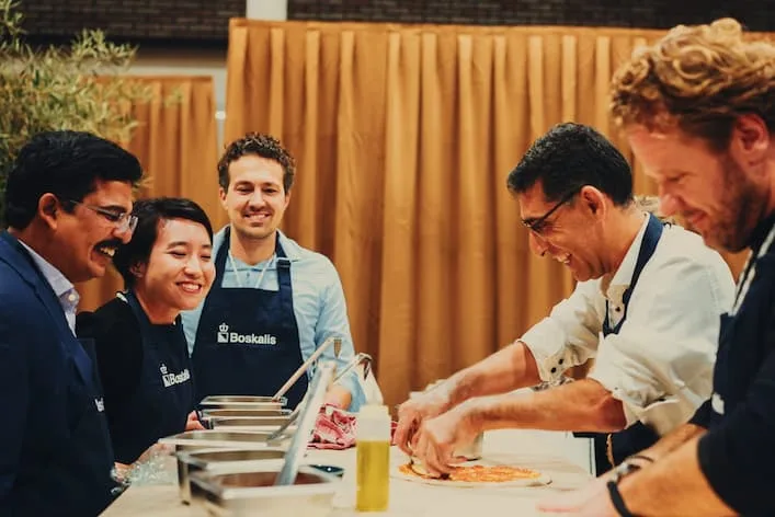 Vijf collega's in schort beleggen lachend samen een pizza