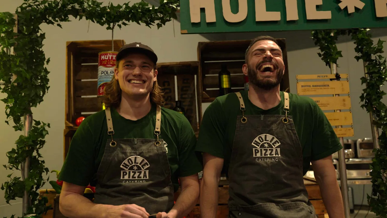 Twee pizzabakkers van Holie Pizza lachen achter hun kraam