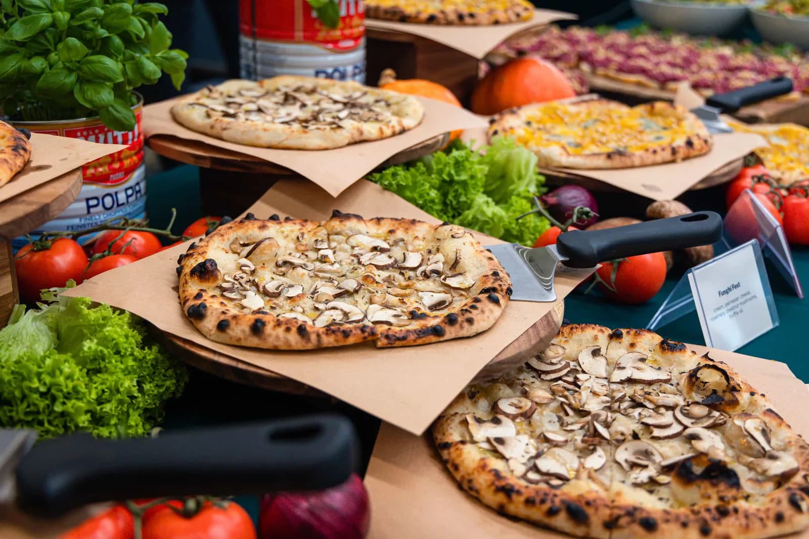Buffet met versgebakken pizza's op houten plateaus, tussen basilicum, tomaten en sla