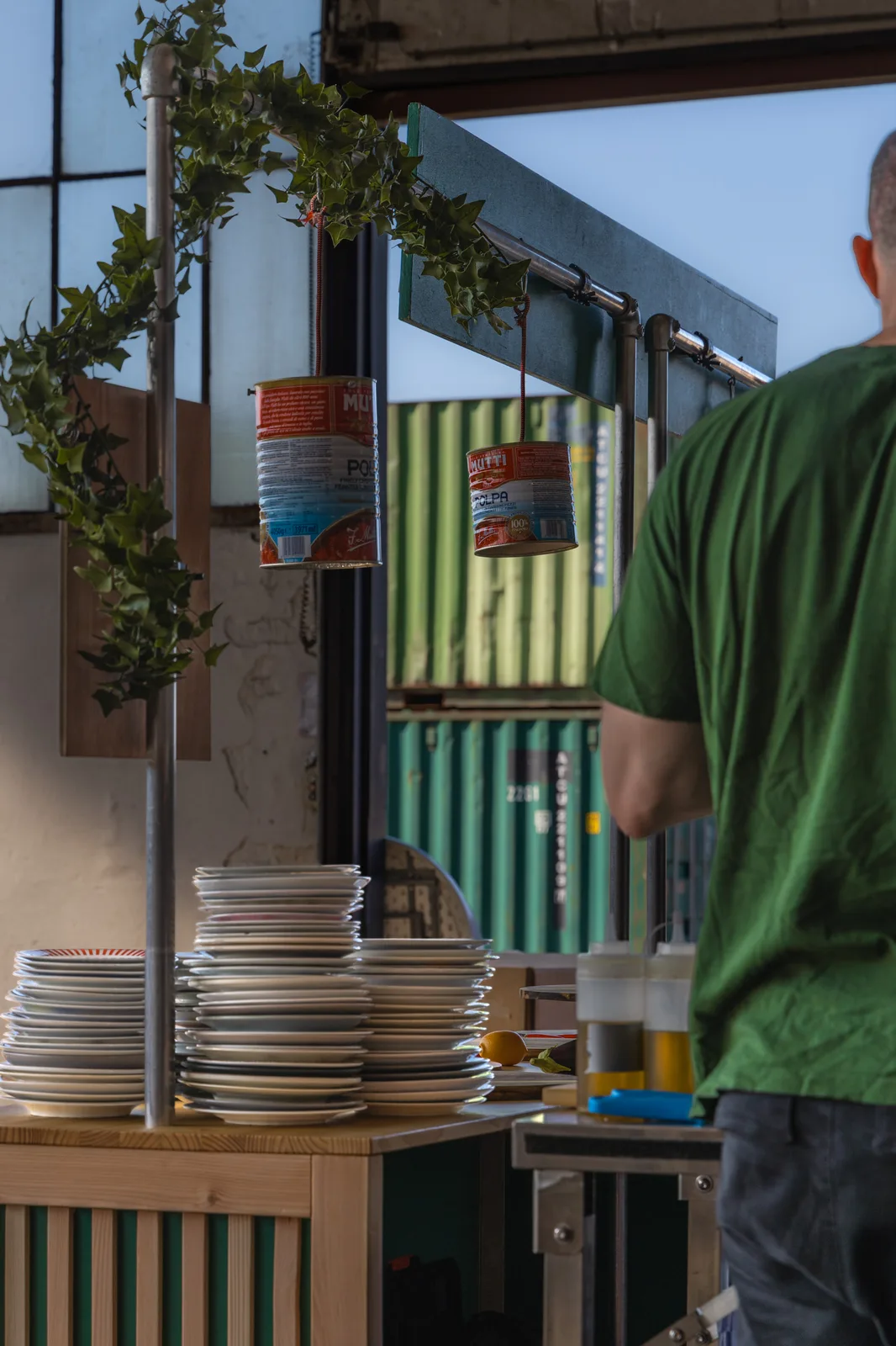 Pizzabakker achter de houten pizzakraam met stapels borden en hangende tomatenblikken